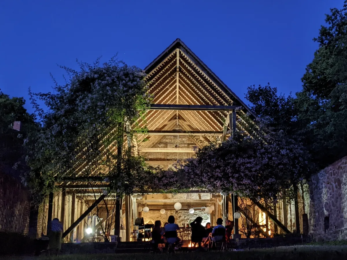 A lit timber barn at dusk, with the team gathered round a fire at its open end